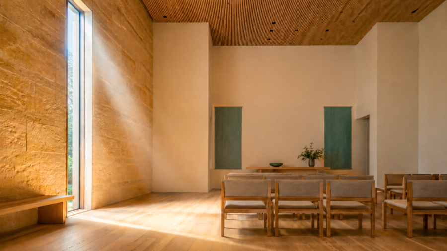 Sunlit memorial gathering hall with limestone wall, wood ceiling, and oak chairs: warm, dignified funeral home design.
