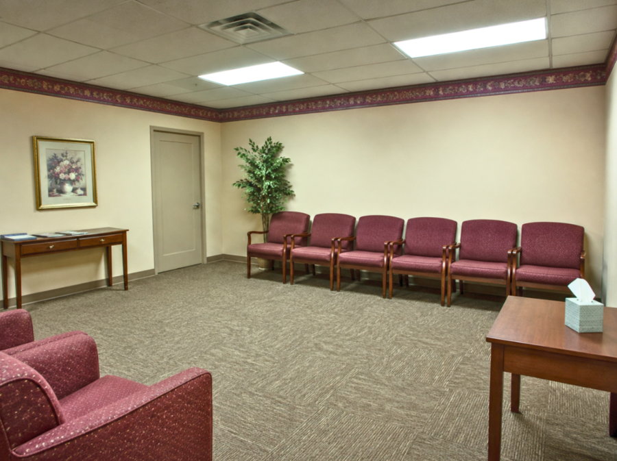 Dated funeral home waiting room with fluorescent lighting, burgundy chairs, and beige walls feeling clinical and cold.