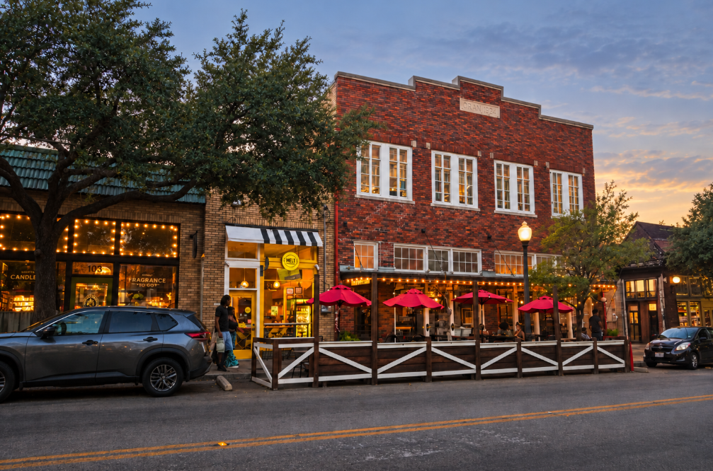 A historic brick building with arched windows on a tree-lined corner as pedestrians pass in late-afternoon light.